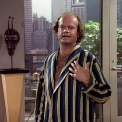 Frasier is making a sarcastic hand gesture illustrating his failing heart due to Martin’s fatty breakfast.