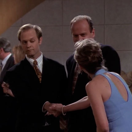 Niles is making a very weird facial expression as he shakes hands with a woman at the party.