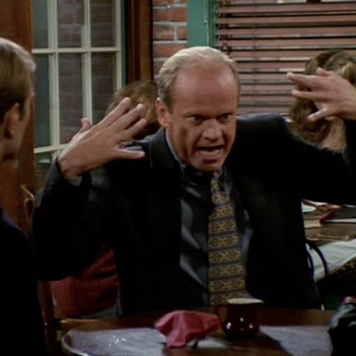 Frasier is making hand gestures and pointing his hands towards his face.